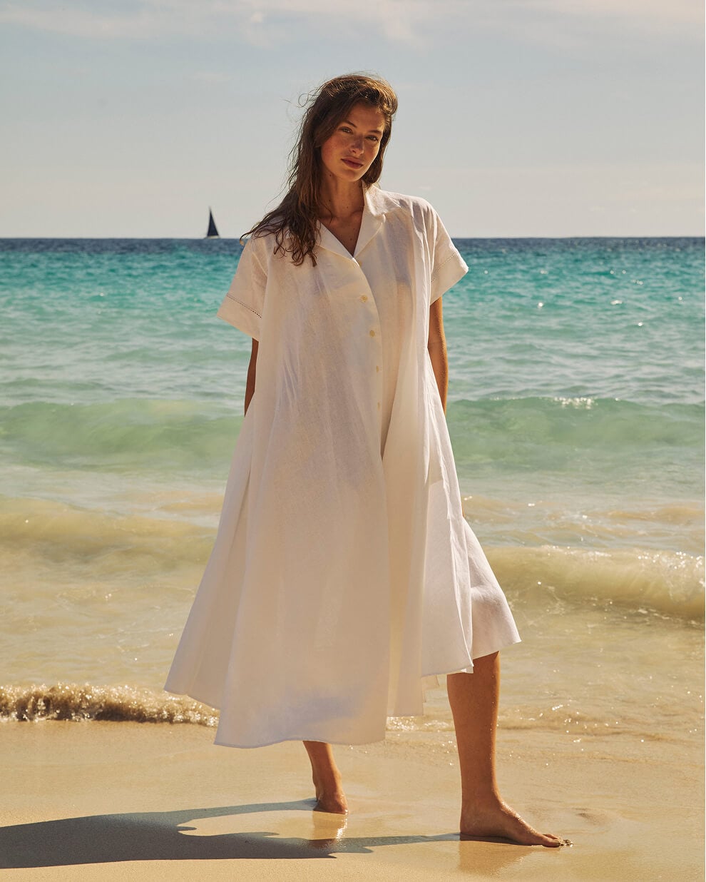 Femme en robe blanche sur plage ensoleillée.